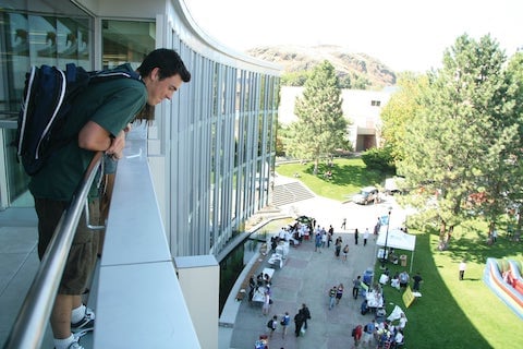 male student on upper floor of building look down at activity on campus