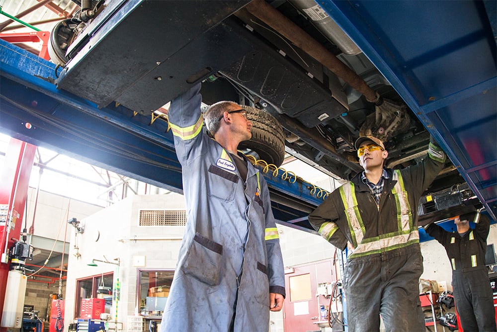 Students working under vehicle on lift