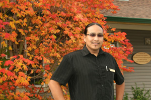 Vernie Clement in front of Gathering House and Fall tree